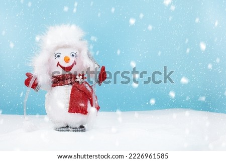 Cute happy snowman wearing fluffy hat and red scarf standing in the snow. Cartoon, funny. Christmas, New year background with winter and snowfall. Copy space