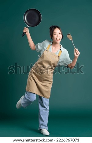 Asian woman wearing apron and holding a pan Royalty-Free Stock Photo #2226967071