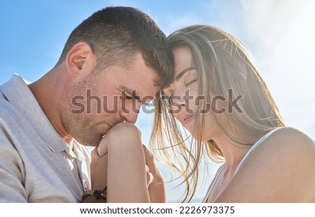 Love, hand and couple kiss at a beach, sharing intimate moment of romance at sunrise against blue sky background. Travel, freedom and man with woman embrace, care and relax in nature together mockup