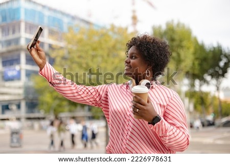 African american curvy young woman drinking a disposable coffee and takes a selfie with the smartphone in the street