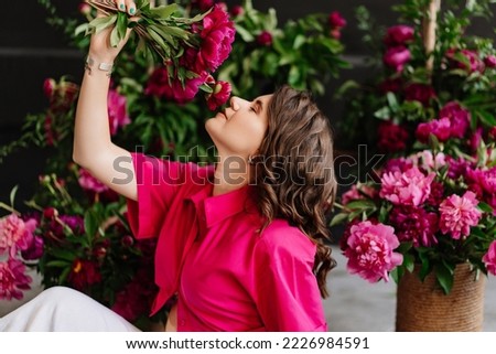 an attractive young woman in a pink blouse with peony flowers. flower shop. training as a florist. perfumes for the body and home. the beauty of flowers.