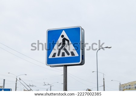 Blue triangle pedestrian crossing sign on blue sky background. A road sign indicating a pedestrian crossing. road sign against the sky.