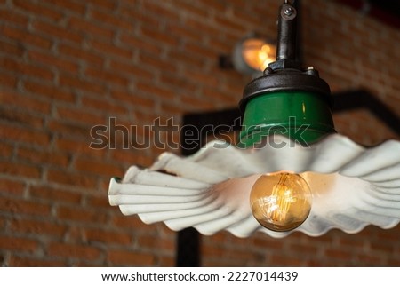 An electric lighting bulb in classic style with round shape of the lamp's part, it turning-on in orange warm light shade. Interior decoration object photo. Close-up and selective focus.