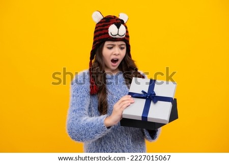 Shocked amazed face, surprised emotions of young teenager girl. Surprised teenage child holding gift box on yellow isolated background. Gift for kids birthday. Christmas or New Year present box.