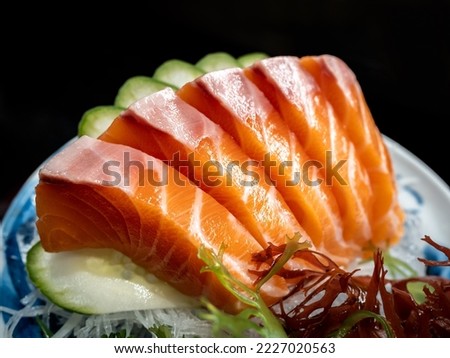 Fresh salmon sashimi, famous japanese food. Five pieces of orange color raw fish Served with cucumber on ceramic plate on dark background. Close-up salmon meat texture.