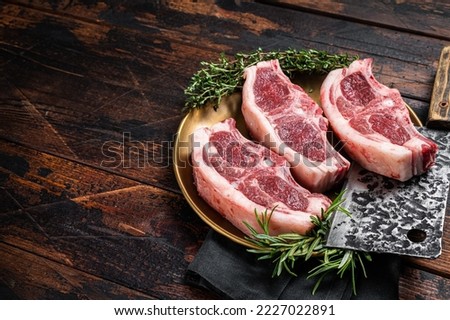 Uncooked Raw lamb loin chops steaks, saddle in plate with rosemary and thyme. Wooden background. Top view. Copy space.