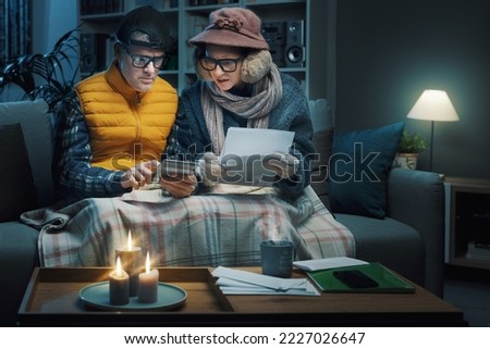 Desperate couple feeling cold at home, they are reading expensive utility bills and checking costs with a calculator