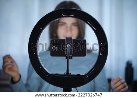 Young creative woman live streaming a video for her followers on social media, she is using her smartphone and a ring light Royalty-Free Stock Photo #2227026747