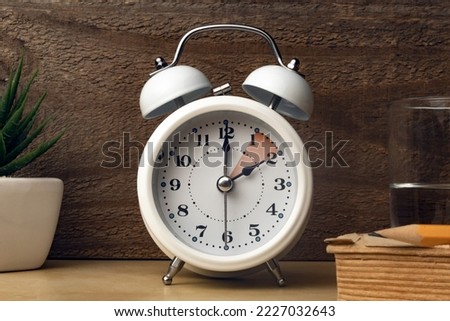 Daylight saving time concept: an alarm clock placed on a bedside table with an indication to move the hands backward Royalty-Free Stock Photo #2227032643