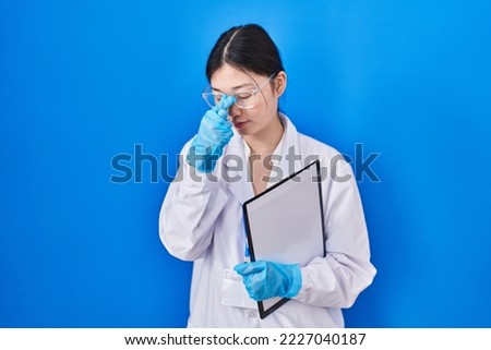 Chinese young woman working at scientist laboratory tired rubbing nose and eyes feeling fatigue and headache. stress and frustration concept. 