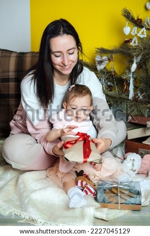 Boxing day and unpacking Christmas gift boxes. Cute Little baby toddler girl and mom unpack gift boxes near the Christmas tree at home. Merry Christmas and a Happy New Year