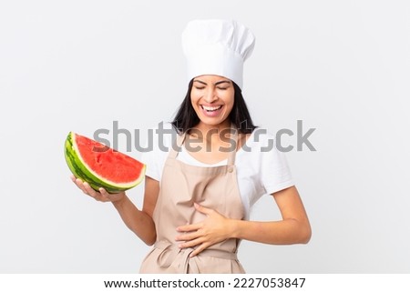 pretty hispanic chef woman laughing out loud at some hilarious joke and holding a watermelon