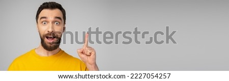 excited bearded man showing idea gesture while looking at camera isolated on grey, banner