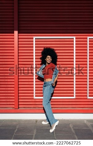 Cheerful african woman with afro hair having fun and posing against red background.