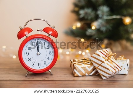Red alarm clock and white gift boxes tied golden ribbons and bow on wooden background. Merry Christmas and Happy New Year holiday greeting card. Copy space