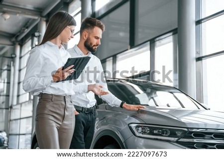 Touching the automobile surface. Man with woman in white clothes are in the car dealership together. Royalty-Free Stock Photo #2227097673