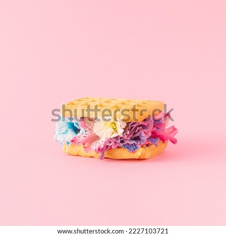 Creative aesthetic arrangement made of waffles and colorful flowers on a pink background. Minimal spring concept. Food and freshness inspiration.