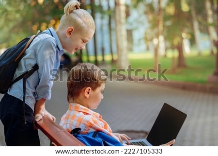 cute caucasian boys sitting on bench in park with laptop computer .Doing homework outdoors after school