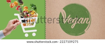 Vegan food online grocery shopping: hand holding a shopping cart icon full of vegetables and fruits