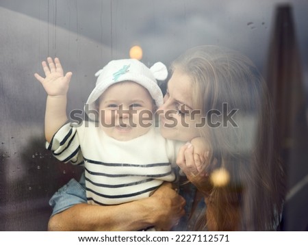 A mother embracing her cheerful child behind the glass window Royalty-Free Stock Photo #2227112571