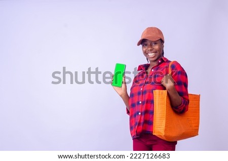 Stylish young african american woman in summer outfit posing with purchases, showing cell phone with green empty screen