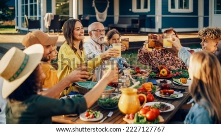 Family and Multiethnic Diverse Friends Gathering Together at a Garden Table Dinner. Old and Young People Raising and Clinking Glasses with Fresh Orange Juice and Celebrating the Occasion. Royalty-Free Stock Photo #2227127767