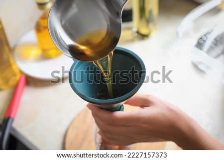 Woman pouring used cooking oil into bottle through funnel in kitchen, closeup Royalty-Free Stock Photo #2227157373