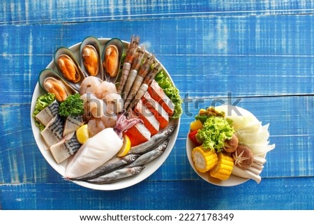 Set of Fresh raw fish and seafood with bowl of mix vegetables prepared for Grill on blue vintage wooden background.