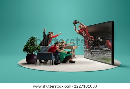 Live stream game. Group of friends sitting in front of huge 3D model of TV screen at home interior and watching online broadcast of american football match. Presence effect Royalty-Free Stock Photo #2227181033