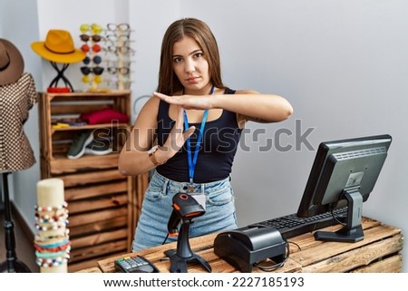 Young brunette woman holding banner with open text at retail shop doing time out gesture with hands, frustrated and serious face 