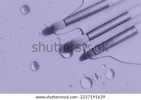 Digital Lavender Color of the Year 2023. Makeup brushes with water drops on a light purple background. Photo is toned of 2023 trendy color.