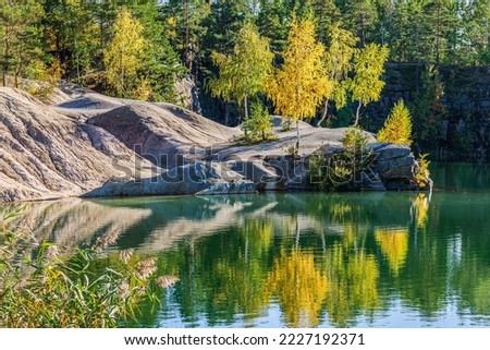Yellow birch trees are reflected in the water of a flooded granite quarry. Korostyshiv Ukraine

