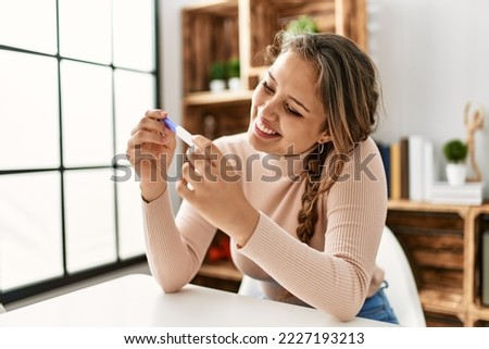 Young beautiful hispanic woman smiling confident holding pregnancy test at home Royalty-Free Stock Photo #2227193213