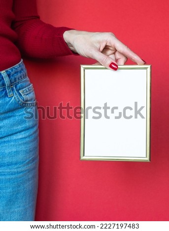 The hands of a white woman in red holding golden frame over a red background