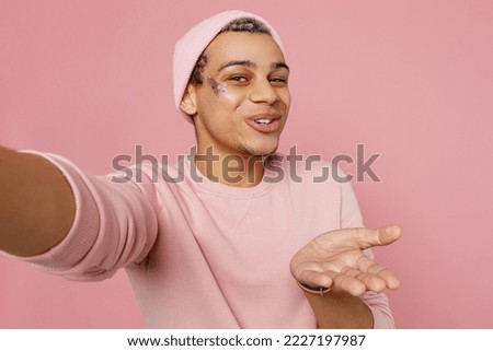 Close up fun young gay man wear sweatshirt hat do selfie shot pov on mobile cell phone blow air kiss isolated on plain pastel light pink color background studio portrait. Lifestyle lgbtq pride concept