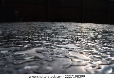 Large water droplets on top of a glass sheet. Against black background. Sunlight reflected and refracted. Enigmatic minimalist monochrome abstract texture and pattern. Alien event horizon singularity