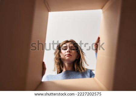 Beautiful woman opening cardboard box relaxed with serious expression on face. simple and natural looking at the camera. 