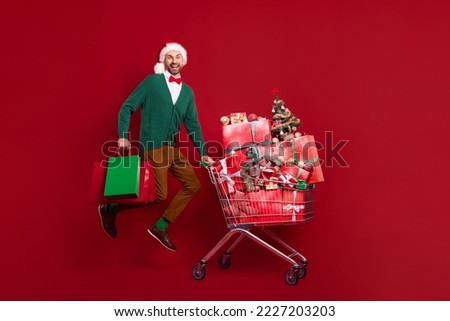 Full length photo of funky jumping air with shopping cart with giftboxes winter season sale hold bags excited isolated on red color background