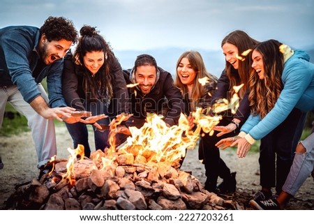 Young friends having fun together at night party around bonfire - Friendship life style concept with happy people traveler making themselves warm by campfire at dusk time - Vivid contrast filter Royalty-Free Stock Photo #2227203261