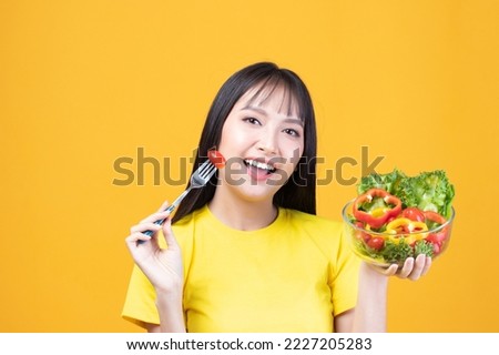 Portrait of happy asian woman eating tasty fresh vegetable salad holding plate bowl and fork on yellow background.