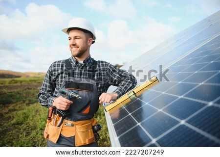 Portrait of smiling confident engineer technician with electrical screwdriver, standing in front of unfinished high exterior solar panel photo voltaic system. Royalty-Free Stock Photo #2227207249