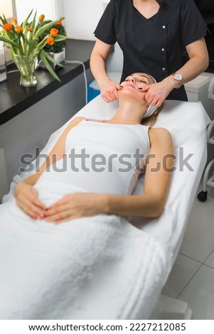 Soon-to-be mother spending her free time at skincare centre. Traditional Japanese face massage performed by unrecognizable caucasian specialist. Vertical indoor shot. High quality photo