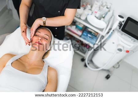 Gentle face massage treatment performed by professional aesthetician. Beauty salon interior. Pretty caucasian woman lying on her back and relaxing. High quality photo