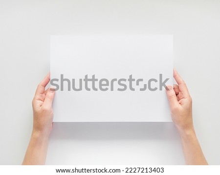 female hands hold an empty white sheet of A4 paper on the background of a white table. empty space for text