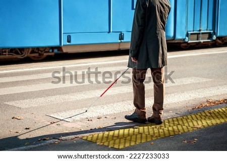 Blind man with a cane stopped on a tactile tile in front of a tram obstacle
