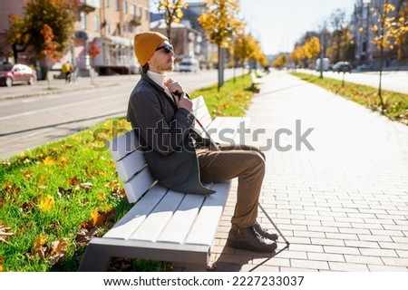 Blind man with a walking stick sitting on a bench in the city