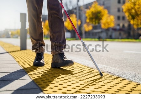 Close-up of a blind man with a walking stick. Walks on tactile tiles for self-orientation while moving through the streets of the city Royalty-Free Stock Photo #2227233093
