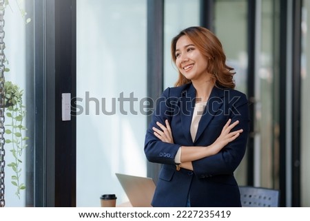Asian businesswoman standing with her arms crossed and confidently looking at the camera and focused on her work in the office.