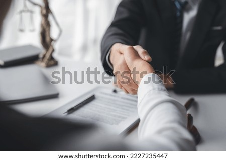 Lawyer shaking hands with a client making about documents, contracts, agreements, cooperation agreements with a female client at the lawyer's desk and a hammer at the table. Royalty-Free Stock Photo #2227235447