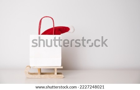 Modern winter holidays background with gift bag on sledge with santa hat in it. Banner with place for text